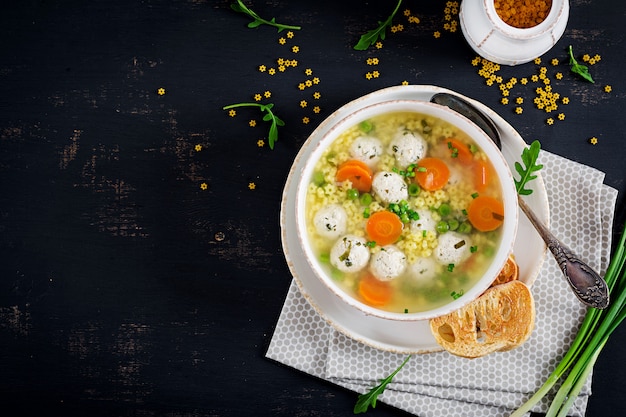 Sopa italiana de albóndigas y pasta Stelline en un tazón sobre la mesa negra.