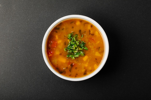 Sopa de lentejas con ingredientes mixtos y hierbas en un tazón blanco.