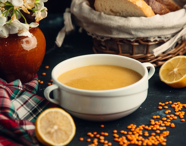 sopa de lentejas servida en un tazón blanco con limones y pan