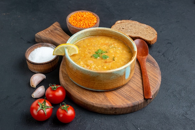 Sopa de lentejas vista frontal con tomates salados y hogazas de pan oscuro sobre una superficie oscura