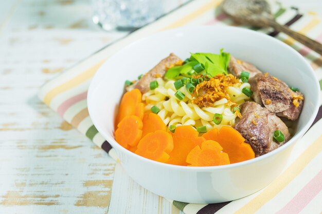 Sopa de macarrones con carne de cerdo y zanahoria en mesa de madera blanca