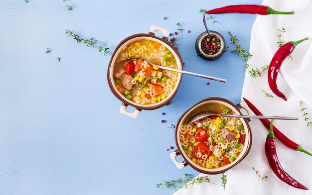 Sopa con pasta pequeña, verduras y trozos de carne en un recipiente en la mesa azul. Comida italiana. Vista superior. Lay Flat