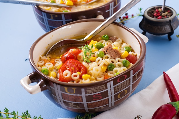 Sopa con pasta pequeña, verduras y trozos de carne en un recipiente en la mesa azul. Comida italiana.