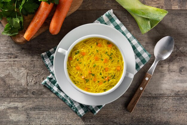 Sopa de pollo con fideos en un tazón blanco sobre una mesa de madera