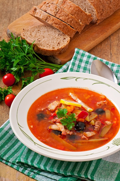 Sopa rusa solyanka con carne, aceitunas y pepinillos en un tazón de madera