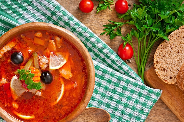 Sopa rusa solyanka con carne, aceitunas y pepinillos en un tazón de madera