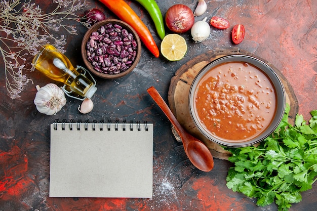 Sopa de tomate clásica con alimentos y botella de aceite de frijoles y un manojo de tomate limón verde y un cuaderno en una mesa de colores mezclados