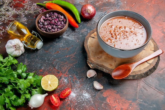 Sopa de tomate clásica con alimentos y botella de aceite de frijoles y un manojo de tomate limón verde en una mesa de colores mezclados