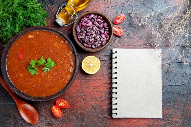 Sopa de tomate clásica en un cuenco marrón, cuchara de frijoles y cuaderno una botella de aceite en la mesa de colores mezclados