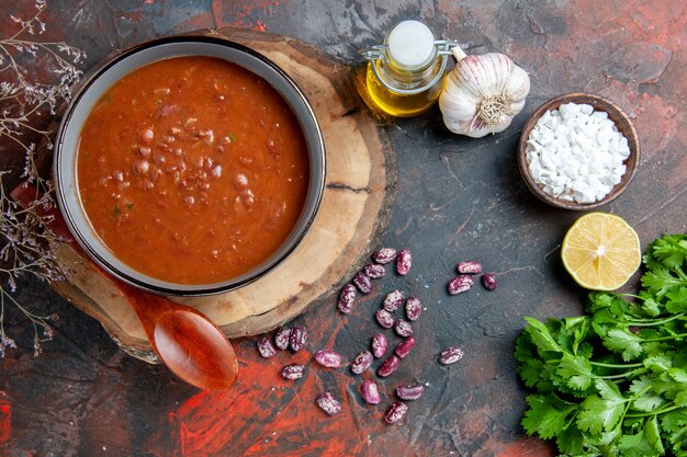 Sopa de tomate clásica en un tazón azul cuchara en bandeja de madera botella de aceite sal de ajo y limón un manojo de verde en la mesa de colores mezclados