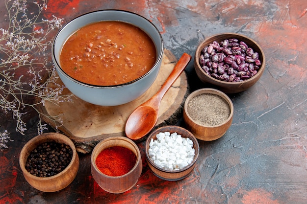 Sopa de tomate con cuchara en bandeja de madera frijoles y diferentes especias en mesa de colores mezclados