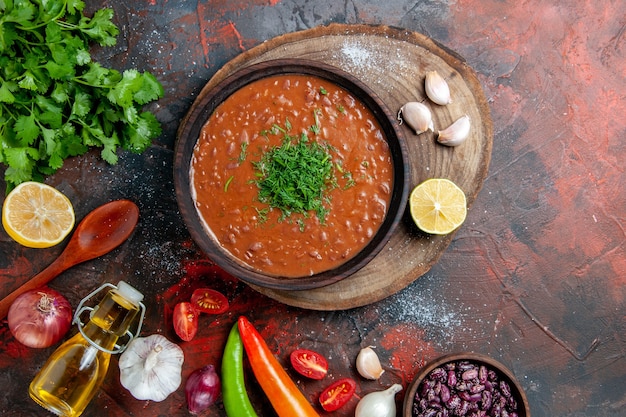 Sopa de tomate con un manojo de ajo verde botella de aceite y una cuchara en la mesa de colores mezclados