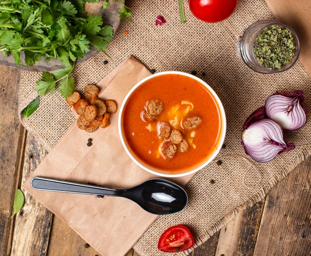 Sopa de tomate con panecillos y queso en un tazón desechable servido con vegetales verdes.