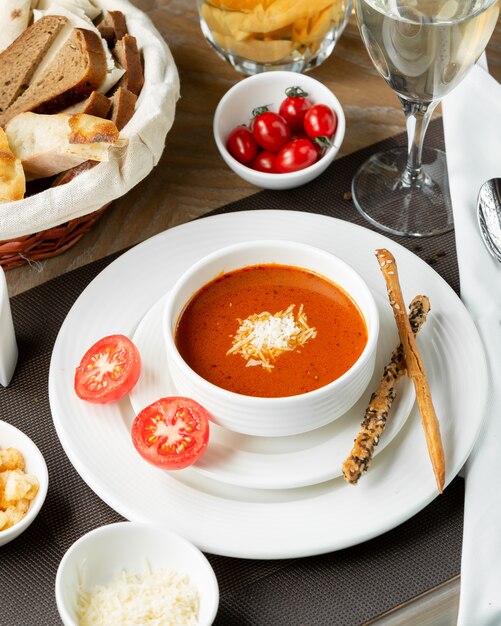 Sopa de tomate con queso picado y palitos de galetta.