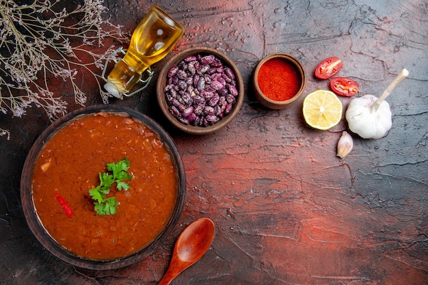 Sopa de tomate en un tazón marrón, pimienta, ajo, limón y frijoles en la tabla de colores mezclados