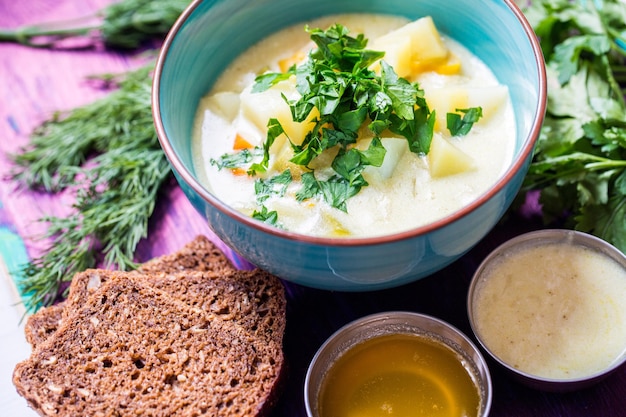 Sopa vegetariana casera con patatas, zanahorias, pimienta con pan oscuro y eneldo sobre fondo de madera