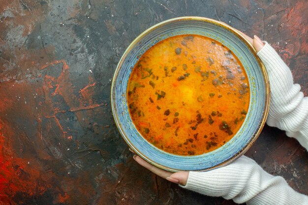 Sopa de vista superior en un tazón azul en manos femeninas en el espacio libre de la mesa rojo oscuro