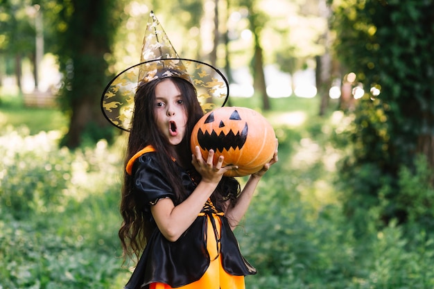 Sorprendente niña en traje de bruja con calabaza