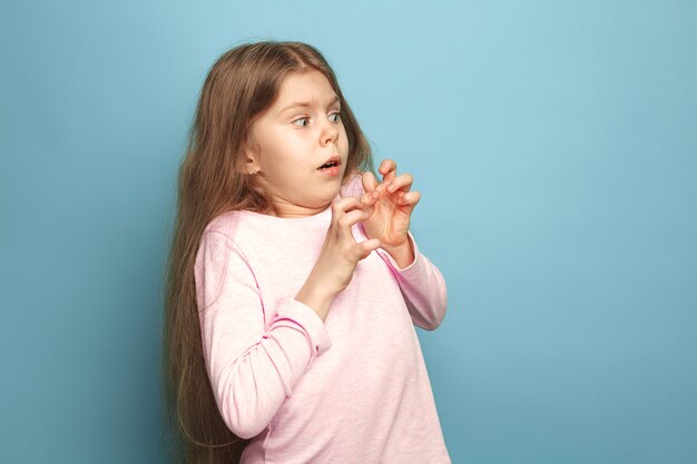 sorprendida asustada muchacha adolescente sobre un fondo azul de estudio. Expresiones faciales y concepto de emociones de personas.