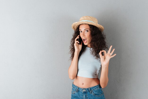 Sorprendida dama con sombrero hablando por teléfono inteligente