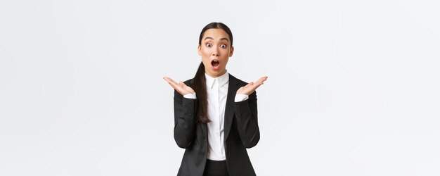 Foto gratuita sorprendida y feliz gerente líder del equipo femenino en la oficina con traje y aplausos sorprendida de escuchar grandes noticias increíble victoria empresaria asiática de pie complacida reaccionando al éxito