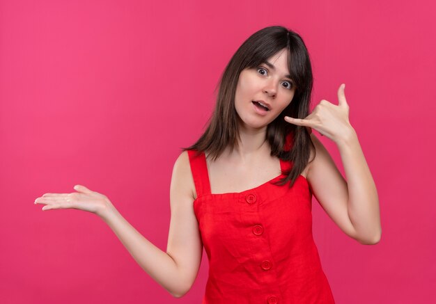 Sorprendida joven caucásica llama gesto de la mano y tiene la mano vacía sobre fondo rosa aislado con espacio de copia