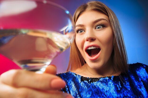 sorprendida joven en ropa de fiesta posando con copa de vino. Cara linda mujer emocional.