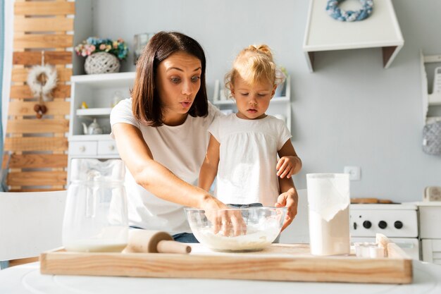 Sorprendida madre e hija pequeña cocinando juntos