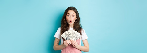 Sorprendida modelo bastante femenina sosteniendo billetes de dólar ganando dinero obtuvo crédito por ir de compras sorprendiendo