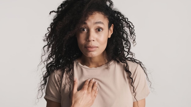 Sorprendida mujer afro de pelo oscuro y esponjoso que muestra la expresión Quién me parece sorprendida aislada en el fondo blanco