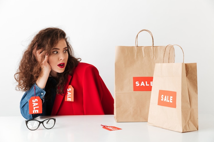 Foto gratuito sorprendida mujer de venta comercial sentada con bolsas de papel