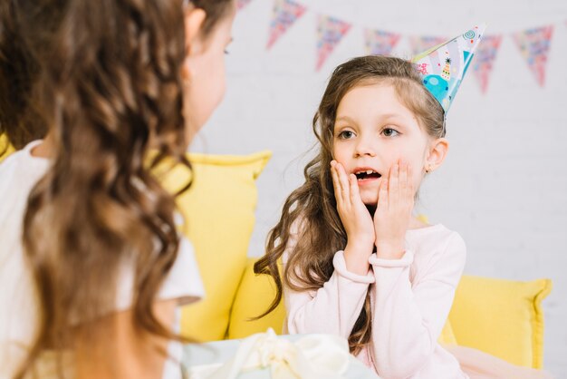 Sorprendida niña de cumpleaños mirando a su amiga sosteniendo presente