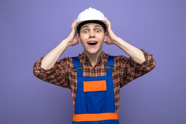 Sorprendido agarró la cabeza joven constructor masculino vistiendo uniforme