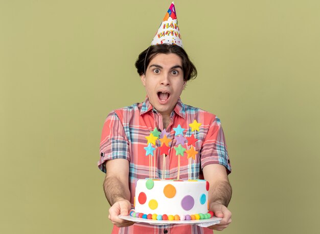 Sorprendido apuesto hombre caucásico vistiendo gorro de cumpleaños tiene tarta de cumpleaños