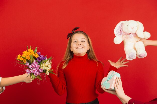 Sorprendido y asombrado. Celebración del día de San Valentín. Feliz, linda chica caucásica aislada sobre fondo rojo de estudio. Concepto de emociones humanas, expresión facial, amor, relaciones, vacaciones románticas.