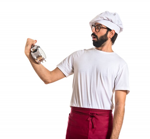 Sorprendido chef sosteniendo un reloj sobre fondo blanco