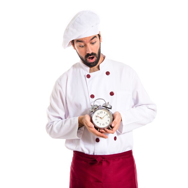 Sorprendido chef sosteniendo un reloj sobre fondo blanco