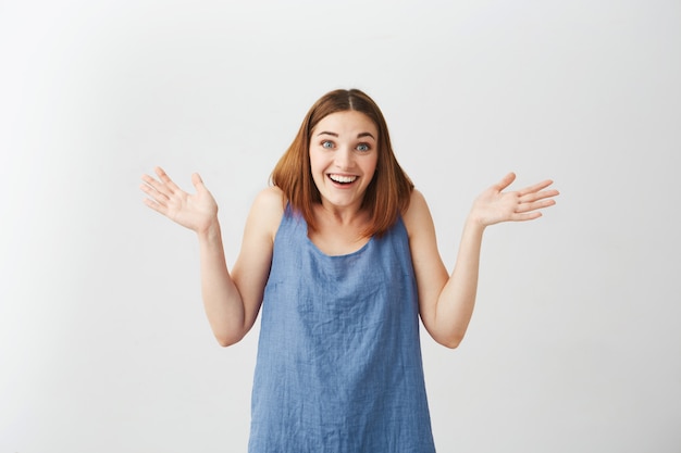 Sorprendido feliz hermosa joven sonriente con la boca abierta encogiéndose de hombros.