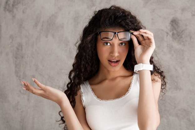 Sorprendido gafas de despegue de mujer de pelo rizado