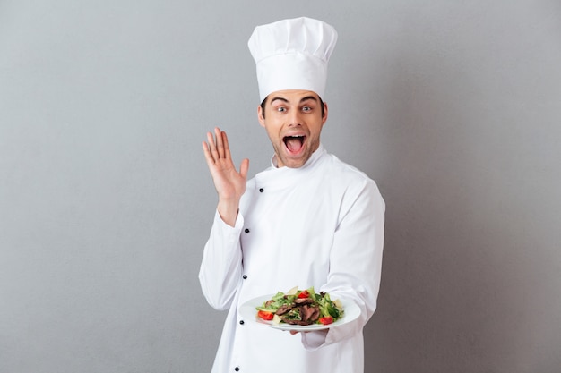 Foto gratuita sorprendido gritando joven cocinero con ensalada.