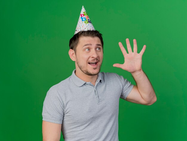 Sorprendido joven fiestero vistiendo gorro de cumpleaños mostrando cinco aislados en verde