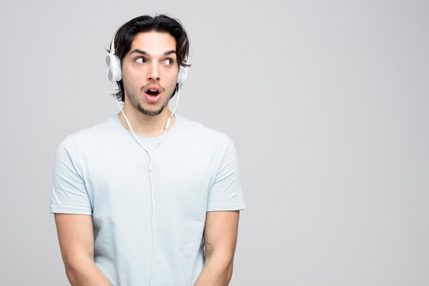 Sorprendido joven guapo con auriculares mirando al lado aislado en fondo blanco con espacio para copiar