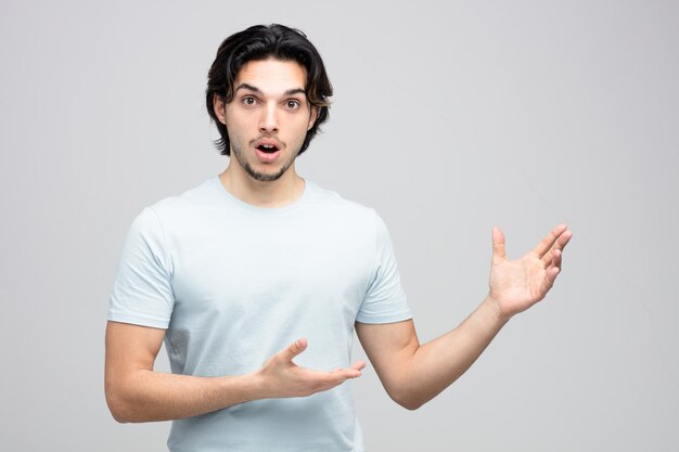 sorprendido joven guapo mirando a la cámara mostrando las manos vacías aislado sobre fondo blanco.