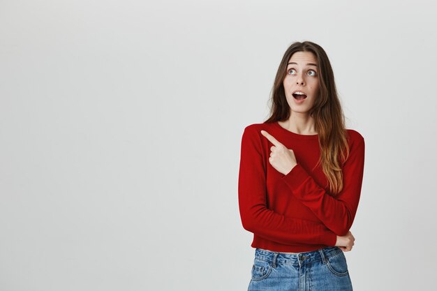 Sorprendido joven mujer bonita señalando y mirando la esquina superior izquierda asombrado