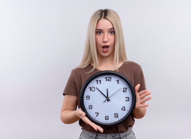 Sorprendido joven rubia sosteniendo el reloj en la pared blanca aislada con espacio de copia