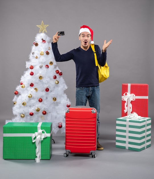 sorprendido, joven, tenencia, tarjeta, posición, cerca, árbol de navidad, y, presenta, en, gris