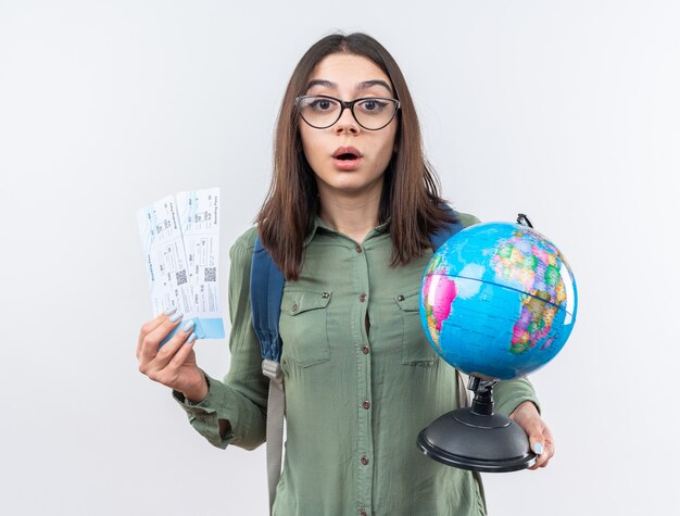 Sorprendido joven viajero mujer con gafas con mochila sosteniendo globo con boletos