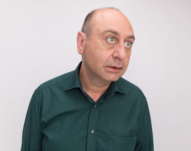 Sorprendido mirando al lado del hombre de mediana edad con camiseta verde aislado en la pared blanca