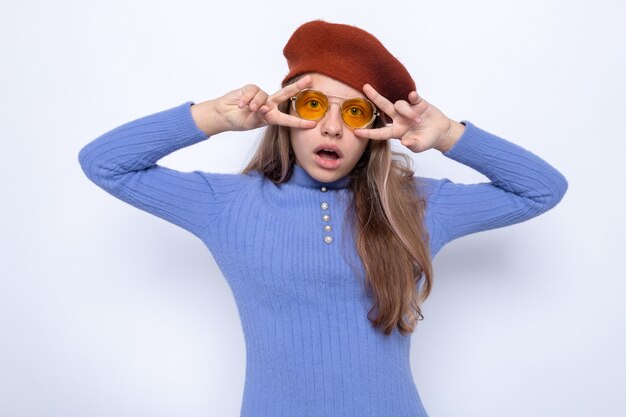 Sorprendido mostrando gesto de paz hermosa niña con gafas con sombrero