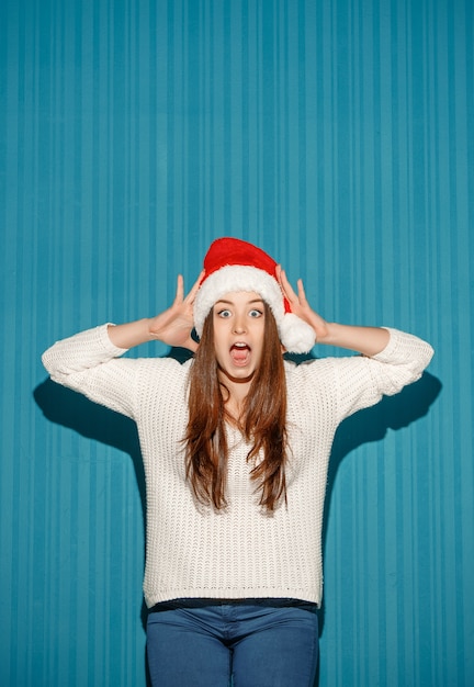 Sorprendido niña de Navidad con un gorro de Papá Noel en el fondo azul del estudio